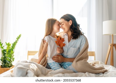 A nice girl and her mother enjoying sunny morning. Good time at home. Child wakes up from sleep. Family playing on the bed in the bedroom. - Powered by Shutterstock