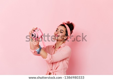 Nice girl in pink pin-up style makes photo on mini camera on isolated background