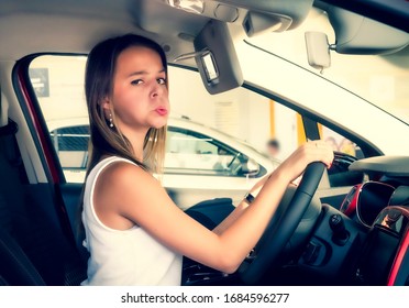 Nice Girl Sitting In The New Car In The Showroom. Buying New Cars Concept. Beautiful Young Woman Grimacing Sad Looking At Camera