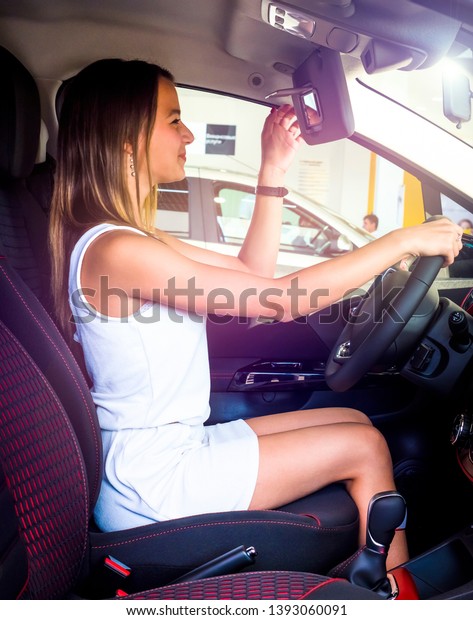 Nice girl sitting in the new car in the showroom\
Buying new cars concept. young woman looking in the mirror.Process\
of testing vehicle.
