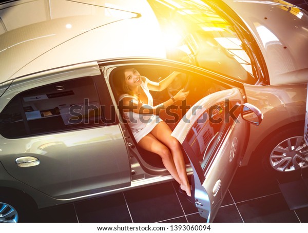 Nice girl sitting in the new car in the showroom.\
Buying new cars concept