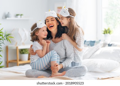 Nice girls and their mother are enjoying sunny morning. Good time at home. Children waking up from sleep. Family playing on the bed in the bedroom. 