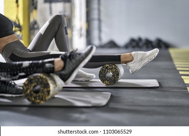 Nice girls are training with black-yellow foam rollers on the gray mats in the gym. They are wearing the multicolored sportswear: pants, tops and sneakers. Closeup. Horizontal.