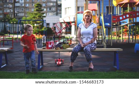 Nice grandmother and her cute little grandson on playground outdoor in morning