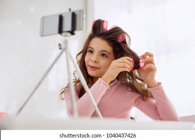 Nice hair volume. Charming pre-teen girl curling her hair with the help of hair rollers and showing how to it correctly while recording a beauty vlog