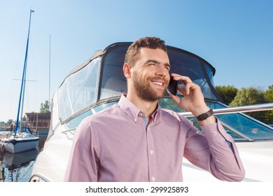 Nice To Hear You. Cheerful Smiling Man Holding Mobile Phone Near His Ear While Having Brisk Conversation Near His Yacht