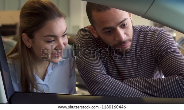 Nice interracial couple looking inside the car at the\
dealership. Close up of handsome african american man showing his\
girl something inside the vehicle. Attractive brunette guy pointing\
his hand on