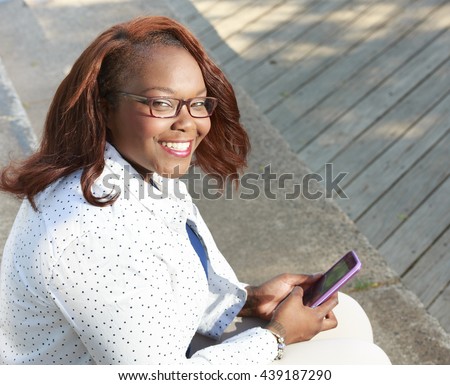 Nice lifestyle shot of a plus size african american woman outside in a casual outfit using a smart phone