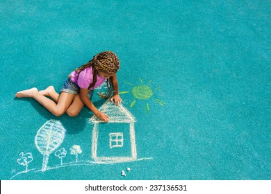 Nice Looking Black Girl Drawing House Sun And Trees With Chalk On Playground 