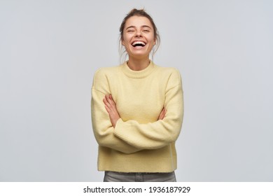Nice looking woman, beautiful girl with blond hair gathered in bun. Wearing yellow sweater. Laughing with eyes closed and arms crossed on a chest. Stand isolated over white background