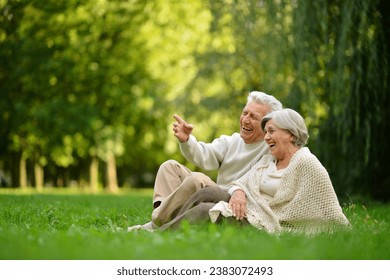 Nice mature couple sitting on green grass in summer park. Woman pointing with finger. - Powered by Shutterstock