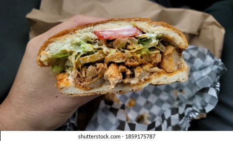 A Nice Mexican Style Chicken Torta Sandwich With Lettuce, Onions, Tomatoes And Sauce Ready To Eat With A Paper Bag And Parchment Wrap In Background.