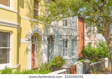 Nice Neighbourhood. Colorful pastel terraced houses in a row, in classic architectural English style, with trees at the street. Diversity concept. Dream upper middle-class community.