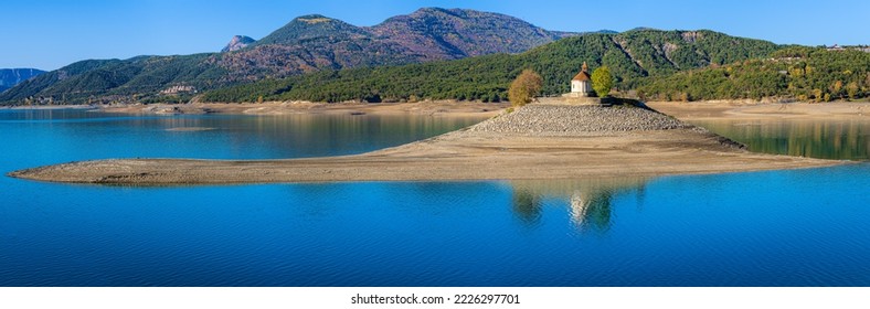 
Nice panorama on a splendid mountain lake, with an isolated chapel on a small island, in the middle of the lake. Low water levels due to global warming. Serre-Ponçon lake, French Alps. - Powered by Shutterstock