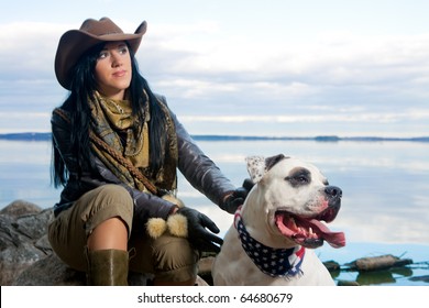 nice and peaceful caucasian brunette girl in stetson and cowboy clothes sitting with her dog in front of seaside and dreaming. dog with american flag neckpiece. shoot made on location with stobes. - Powered by Shutterstock