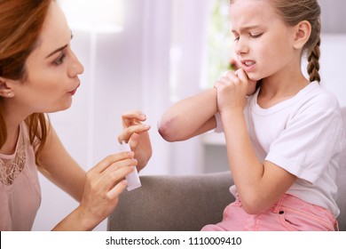 Nice Pleasant Woman Looking At Her Daughters Bruise While Applying Ointment On It