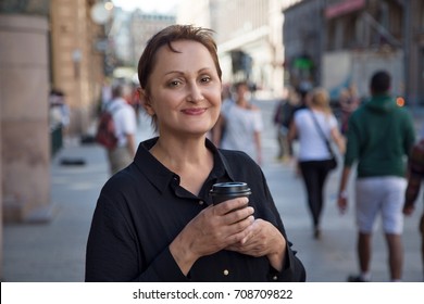 Nice portrait of a middle aged older woman walking in city. Outdoor headshot of 45 50 year old relaxed woman on lunch break drinking coffee. Urban background. Street style shot.