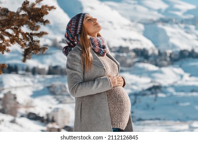 Nice Pregnant Woman With Closed Eyes of Pleasure Enjoying Bright Sun Light in Snowy Mountains. Spending Pregnancy Time in Winter Mountainous Resort.