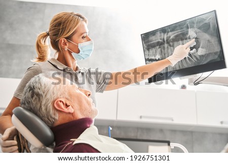 Nice results here. Lovely attentive prominent dentist showing at the x ray and explaining positive tendencies to her senior patient after treating him for some time. Stock photo
