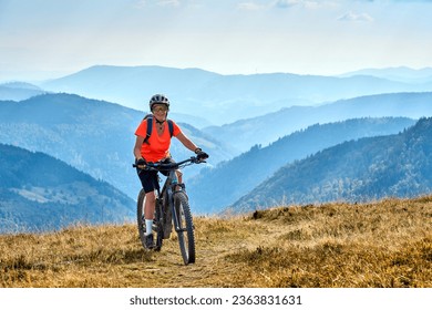 nice senior woman on her electric mountain bike cycling on Feldberg summit with stunning view over the Black Forest mountains and valleys - Powered by Shutterstock