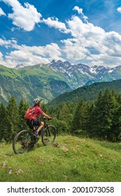 nice senior woman on mountain bike climbing up Mount Fellhorn in the Allgaeu High Alps with Trettach and Maedelegabel in background, Allgau, Bavaria, Germany, landscape

