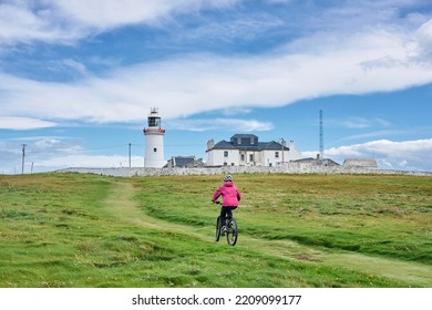 nice senior woman on mountain bike, cyclingat Dunmore Head Lighthouse near Kilballyowen , County Limerick in the southwestern part of the Republik of Ireland