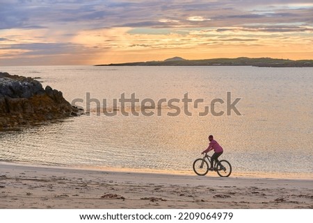 nice senior woman on mountain bike, cycling in sunset at the golden sand beach of Sillerna, Grallagh, County Galway, in the western part of the Republic of Ireland