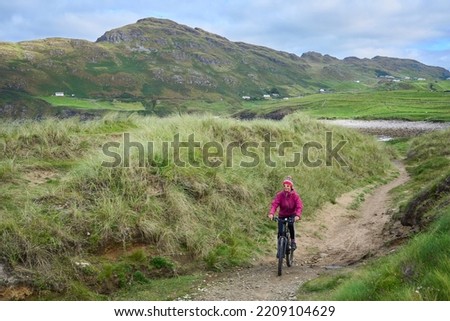 nice senior woman on mountain bike, cycling in dawn light in the dunes of Sillerna, Grallagh, County Galway, in the western part of the Republic of Ireland