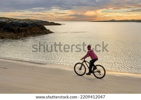 nice senior woman on mountain bike, cycling in sunset at the golden sand beach of Sillerna, Grallagh, County Galway, in the western part of the Republic of Ireland