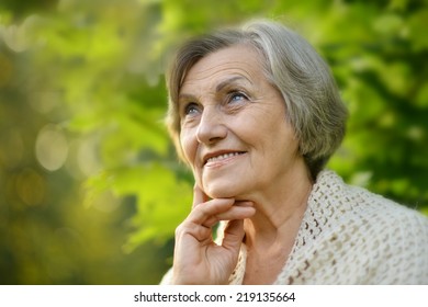 Nice smiling old woman on the green leaves background