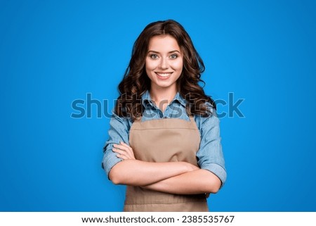 Nice stylish cheerful lovely sweet attractive brunette girl, barista with wavy hair in casual denim shirt and apron, crossed hands, isolated over grey background