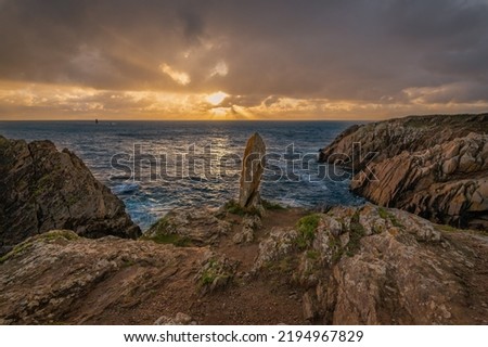 Nice sunset on a cloudy day, on a menhir in front of stone cliffs and the ocean