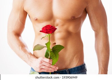 Nice Surprise For Her. Close-up Of Young Muscular Man With Perfect Torso Holding Single Rose While Standing Against White Background 