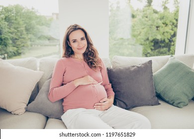 Nice Sweet Tender Adorable Lovely Cheerful Positive Optimistic Surrogate Pregnant Mom In Casual Wear, Sitting On Divan, Touching Belly, Carrying Baby, White Light Interior Room