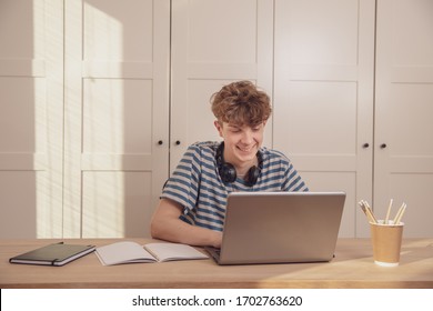 A nice teenage boy in headphones uses a laptop and learns at his desk in his room. Distance learning because of the epidemic coronavirus - Powered by Shutterstock