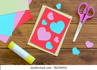 Nice Valentines Day Card With Paper Hearts, Scissors, Glue Stick, Colored Paper Sheets On A Wooden Background. Creative Valentines Day Card Crafts. Easy Paper Craft Projects. Top View