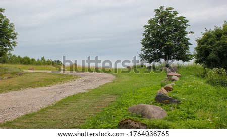 Nice view of a gravel road bend in the countryside in summer. Well-groomed roadside with mowed grass. Beautiful boulders border the road. Latvia.