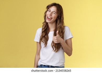 Nice well done mate. Cheerful outgoing cheeky attractive curly-haired female wink smiling nod approval show thumbs up like your choice good job accept terms stand yellow background - Shutterstock ID 2134558265