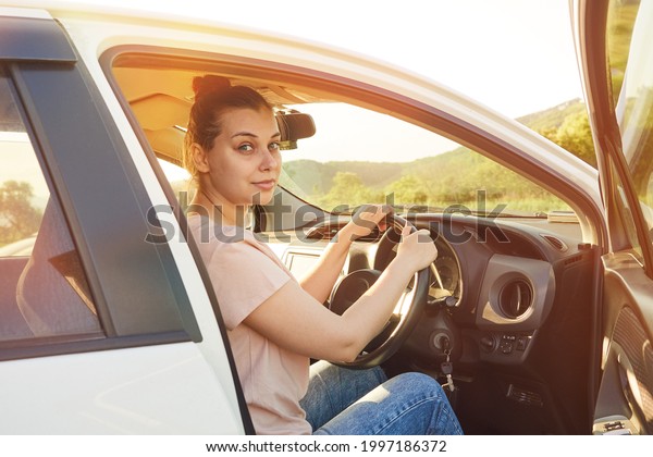 Nice woman sits in the car holding the steering\
wheel with her hands, the door is open, the woman driver is going\
on a trip