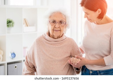 Nice woman supporting pensioner by hand standing in light room