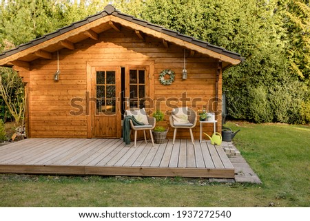 Nice wooden hut in a green garden. Garden shed with chairs and flowers. Spring mood. Drinking tea outside in spring. 