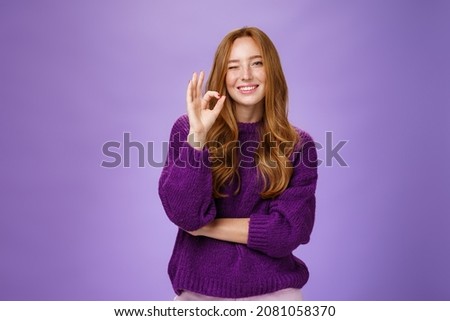 Nice work you did great. Satisfied and happy charming assertive and supportive redhead woman in purple sweater smiling and winking in approval showing okay gesture, liking product over violet wall