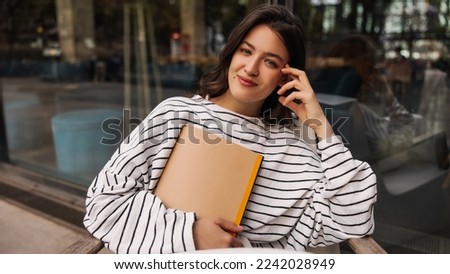 Nice young caucasian girl looking at camera spending time outdoors. Brunette with wavy hair wears sweatshirt. Relaxation concept