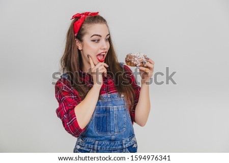 Nice young girl holding big doughnut, looking at it as if ready to eat it at once.