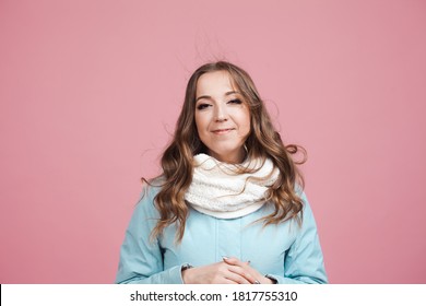 Nice Young Woman In A Blue Winter Jacket And Scarf, Her Hair In The Wind. Portrait On A Pink Background