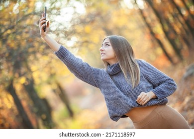 A Nice Young Woman In A Warm Sweater Catches A Call On The Phone In The Autumn Forest. Poor Mobile Network Coverage