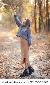 A Nice Young Woman In A Warm Sweater Catches A Call On The Phone In The Autumn Forest. Poor Mobile Network Coverage