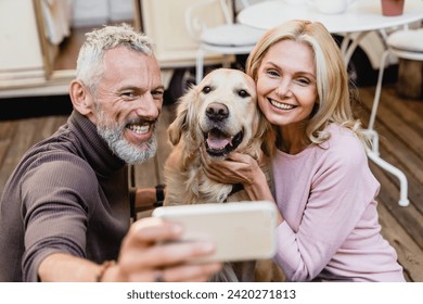 Nice-looking senior caucasian couple taking selfie with their dog on the caravan porch. Vlogging blogging online while traveling with golden retriever by trailer motor home - Powered by Shutterstock