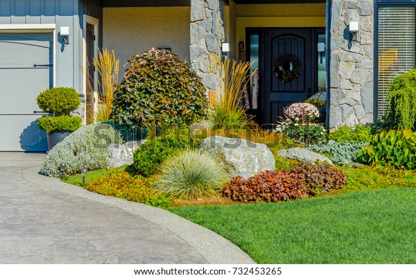 Nicely trimmed bushes and flowers in front of the\
house. Landscape design.