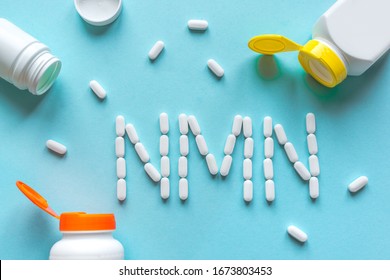 Nicotinamide mononucleotide, niacin, anti adeing vitamin. White pills forming shape to NMN alphabet on blue background, copy space, top view.